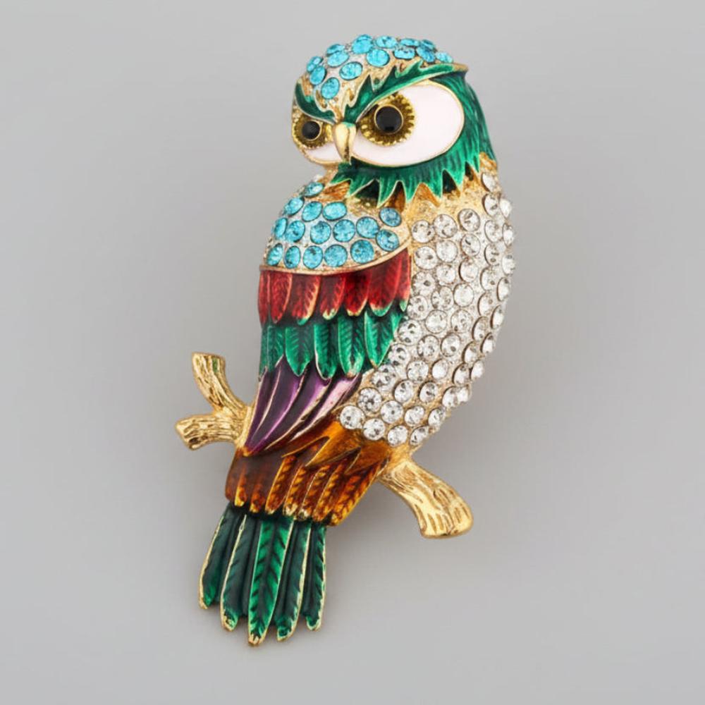 Colorful owl-shaped brooch perched on a golden branch on a light gray  background