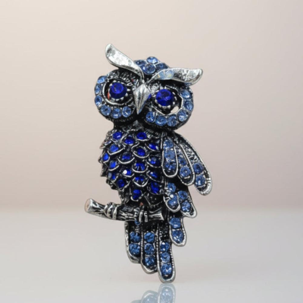Blue rhinestone owl brooch on a silver-tone branch on a light gray background