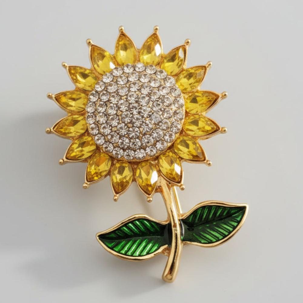 Sunflower-shaped brooch with yellow rhinestone petals, green enamel leaves, and a gold center against a light gray background