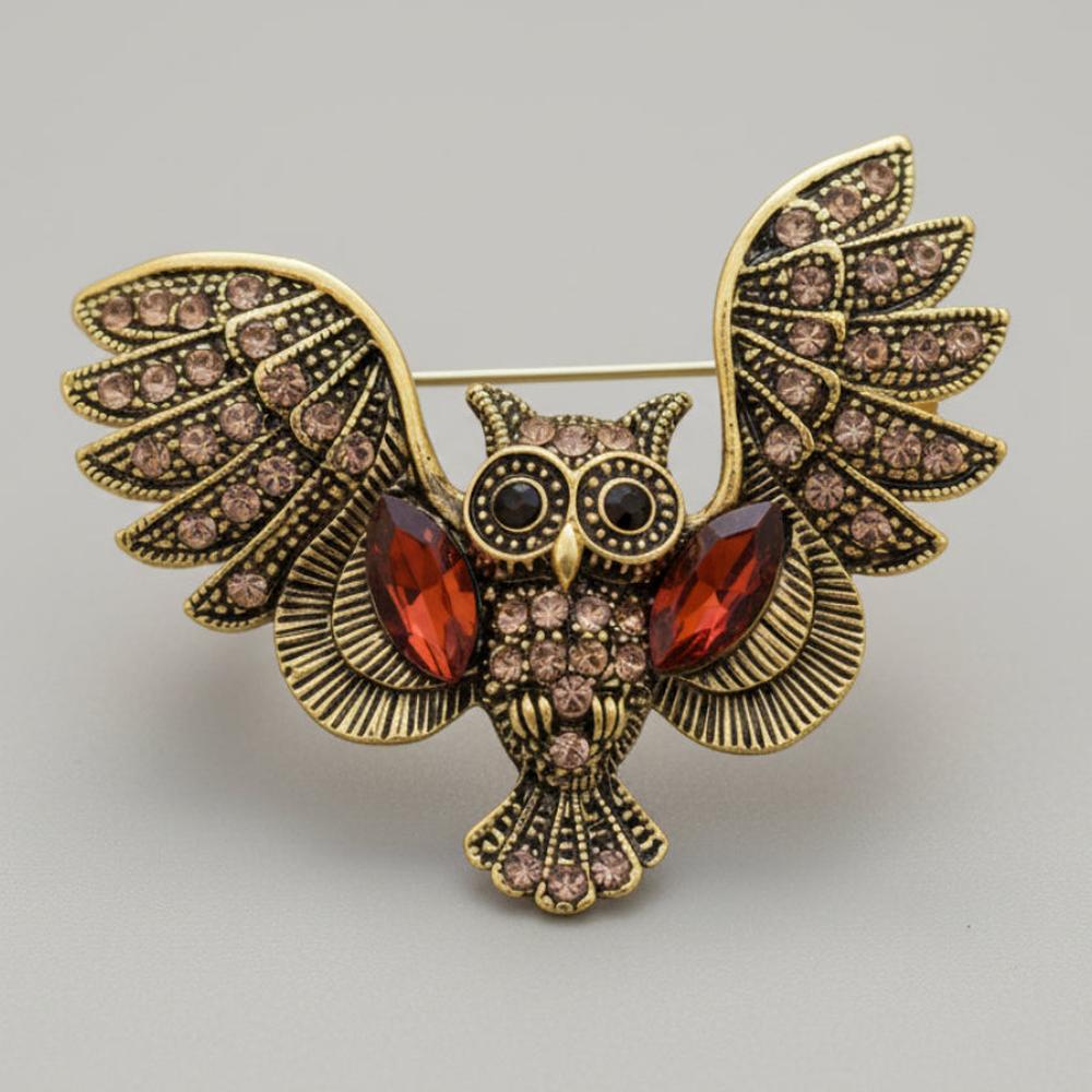 Decorative owl brooch with amber color rhinestones on a light gray background